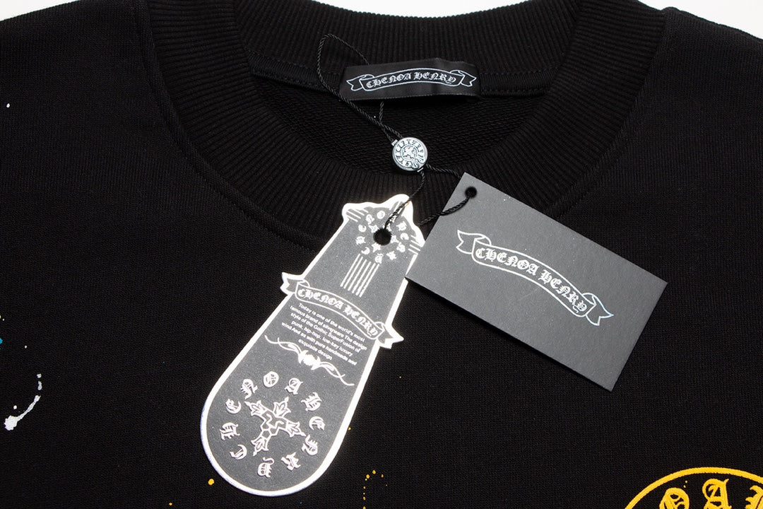 Sweat-shirt noir à motif de cœurs chromés, coulures de peinture et croix jaune.