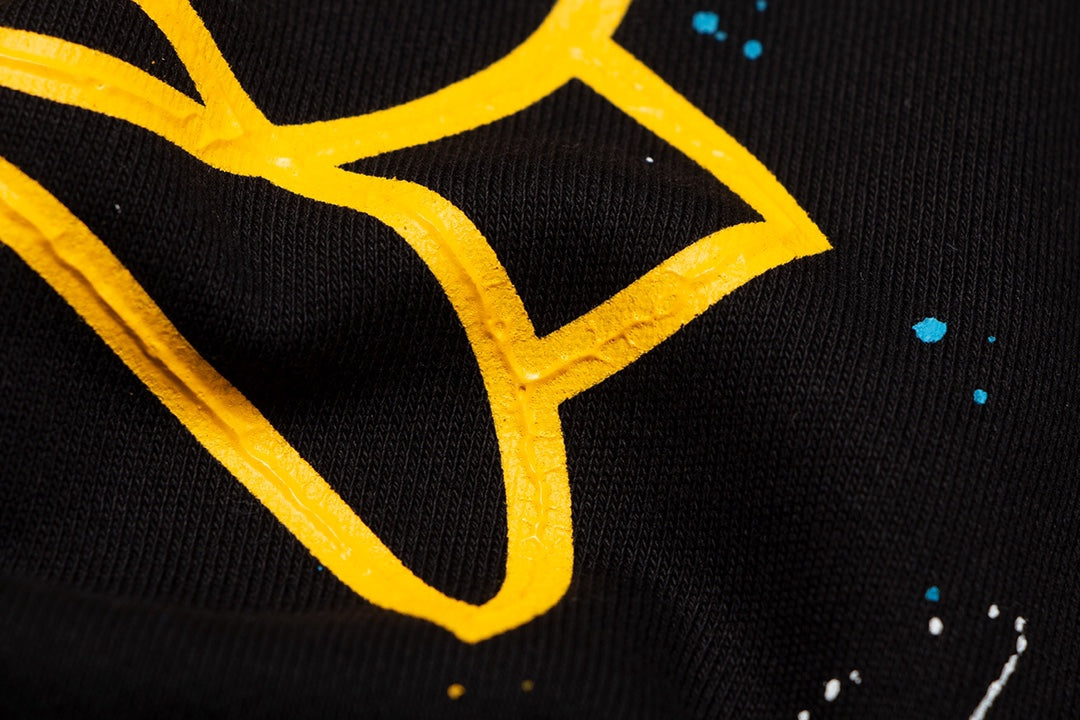 Sweat-shirt noir à motif de cœurs chromés, coulures de peinture et croix jaune.